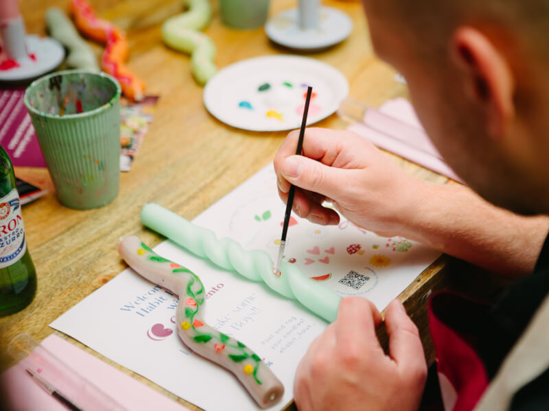 A close up of a person painting motifs on a mint green twisted candle